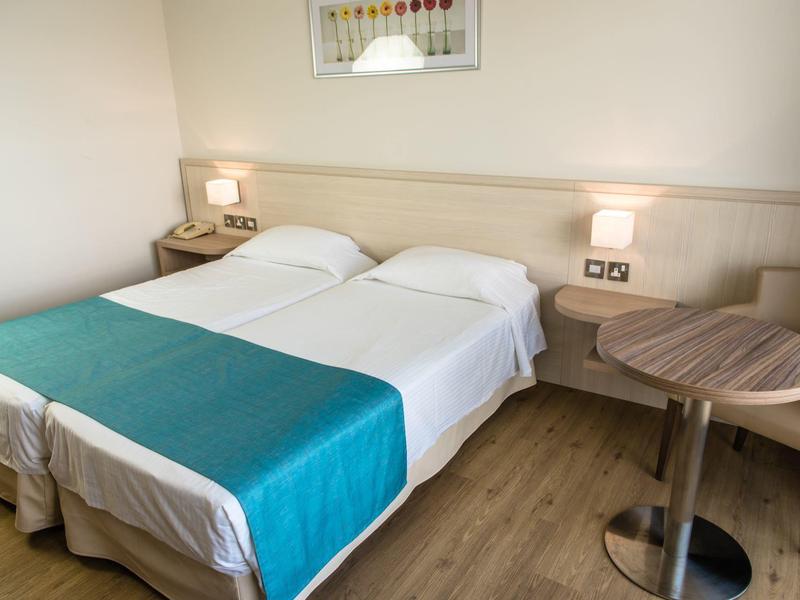 Ein einfaches Hotelzimmer mit zwei Einzelbetten, einem kleinen runden Tisch und einem Stuhl.