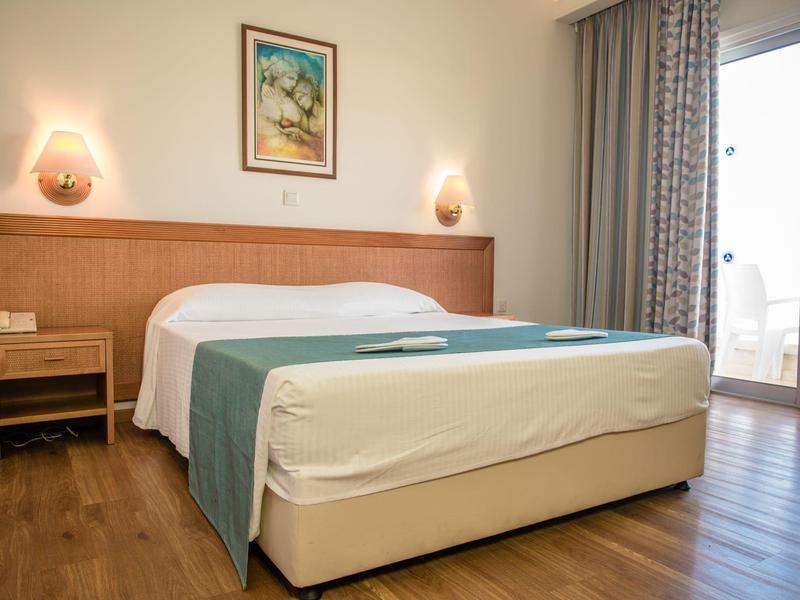 Schlafzimmer mit Doppelbett, Holzboden, Nachttisch, Wandlampen, Bild und Balkon mit Vorhängen.