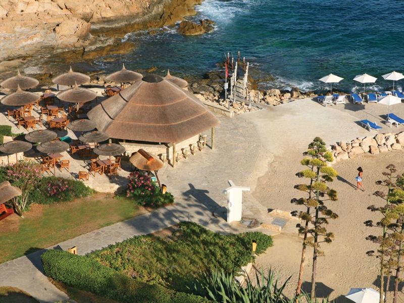 Strand mit sandigem Ufer, Sonnenschirmen, Palmen und runden Strohdach-Bungalows am blauen Meer.