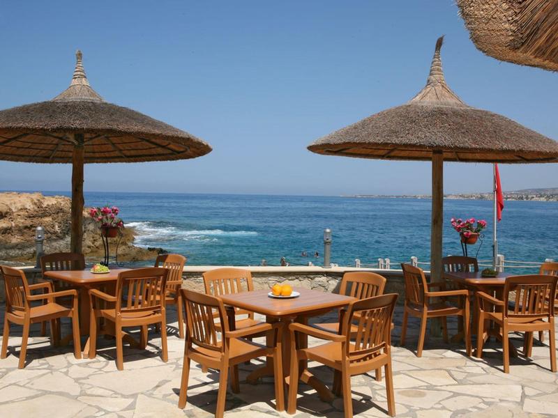 Freiluftterrasse am Meer mit Holztischen und Stühlen unter Strohdächern bei klarem Himmel.