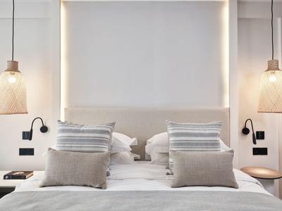 Modernes Schlafzimmer mit Doppelbett, grauen Kissen und zwei hängenden Lampen an den Seiten.