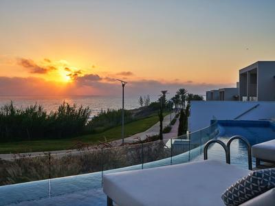 Sonnuntergang über Küstenlandschaft mit Pool und Liegestühlen im Vordergrund.