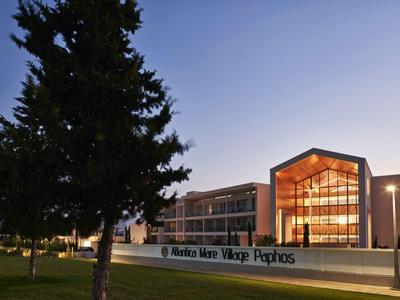 Modernes Gebäude mit großen Glasfenstern neben großem Baum bei Dämmerung.