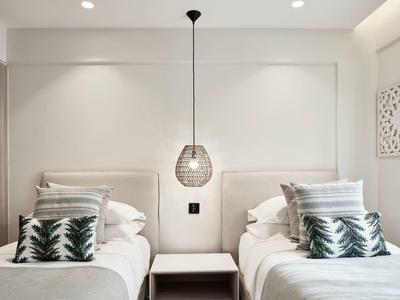 Minimalistisches Schlafzimmer mit zwei Einzelbetten, weißen Wänden, grünen Kissen und Hängeleuchte in der Mitte.