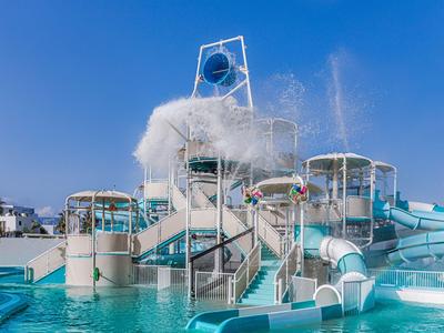 Waterpark met glijbanen, zwembad en fontein onder een blauwe lucht