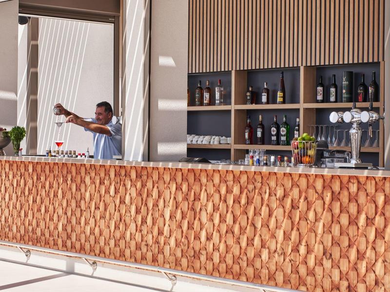 Moderner Außenbarbereich mit Holzverkleidung, Regalen und einem Barkeeper, der Getränke mixt.