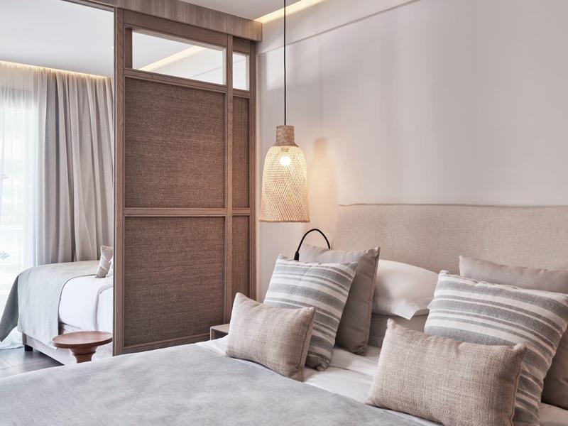 Modernes Schlafzimmer mit hellen Vorhängen, weichen Kissen und Holztrennwand zwischen zwei Betten.