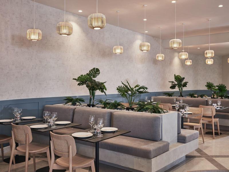 Modernes Restaurant mit grauen Polstersesseln, hölzernen Stühlen und grünen Pflanzen auf Tischen.