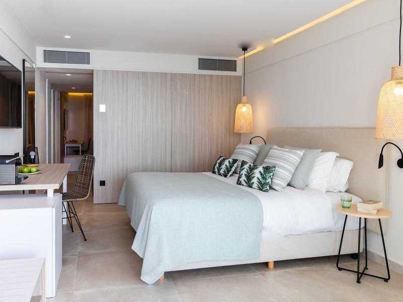 Helles Schlafzimmer mit großem Bett, zwei Nachttischen, TV und moderner Beleuchtung.