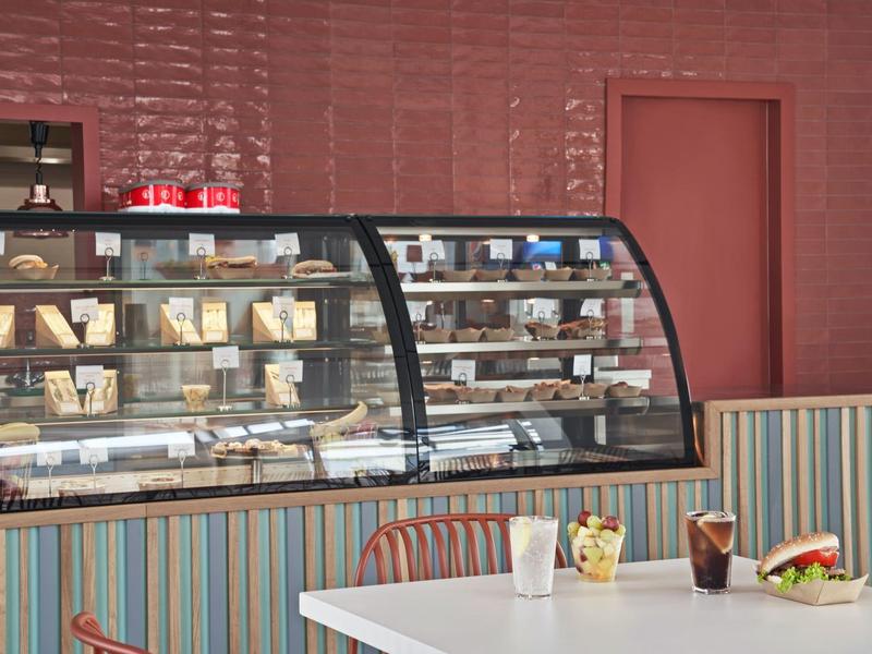 Modernes Café mit Vitrine voller Backwaren, bunten Stühlen und gedecktem Tisch mit Snacks und Getränken.