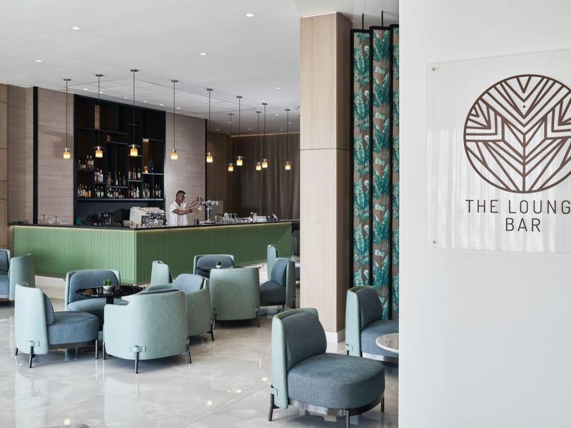 Moderne Lounge-Bar mit grüner Theke, blauen Sesseln und glasigen Hängelampen.