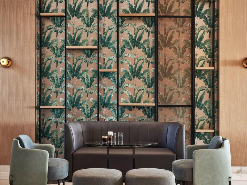 Elegantes Wohnzimmer mit dunkelbraunem Ledersofa, grünen Sesseln und blumenmusterter Wandgestaltung.