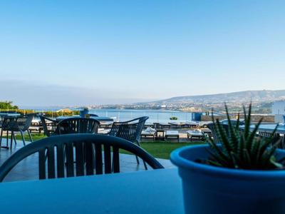 Uitzicht vanaf een terras met planten op de zee en verre heuvels.