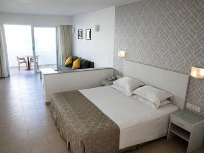 Helles Schlafzimmer mit großem Bett, Nachttisch, gemusterter Wand und Blick auf Balkon mit Meer.