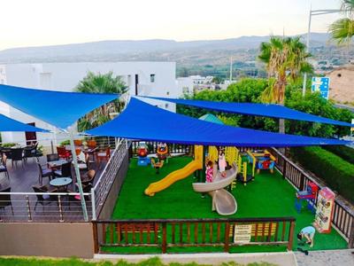 Außenbereich mit blauem Sonnensegel, Spielplatz mit Rutsche und Sitzbereich mit Tischen und Stühlen.