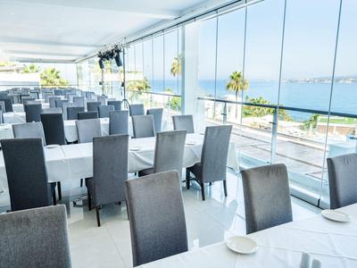 Heller Speisesaal mit Blick aufs Meer und mehreren gedeckten weißen Tischen und grauen Stühlen.