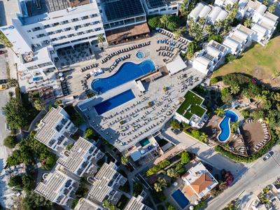 Luftaufnahme eines Hotels mit mehreren Pools, Sonnenschirmen und umgebender Vegetation.