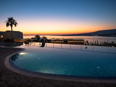 Rundlicher Hotelpool bei Sonnenuntergang mit Blick auf das Meer und eine Promenade.