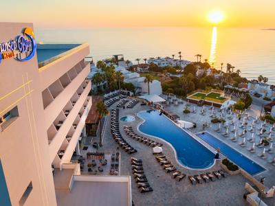 Hotel mit großem Pool und Sonnenliegen, Blick auf das Meer bei Sonnenuntergang.