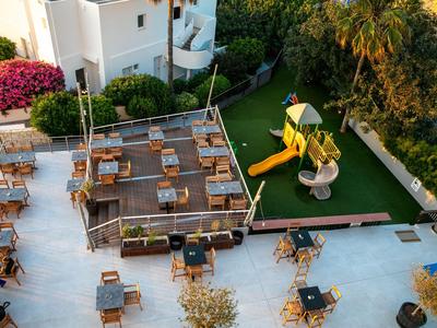 Terrasse mit Tischen, Stühlen und einem kleinen Spielplatz neben einem Hotelgebäude.