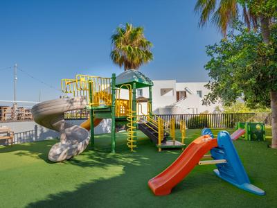 Kinderspielplatz mit Rutschen und Klettergerüsten auf grünem Rasen unter blauem Himmel.