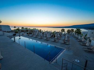 Hotelpool mit Liegestühlen und Palmen bei Sonnenuntergang mit Meerblick.