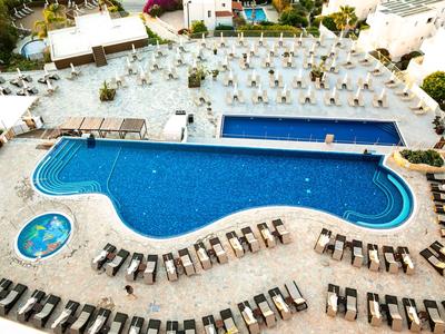 Großer Hotelpool mit blauer Wasserfläche, umgeben von vielen Liegestühlen und einem kleinen runden Pool.