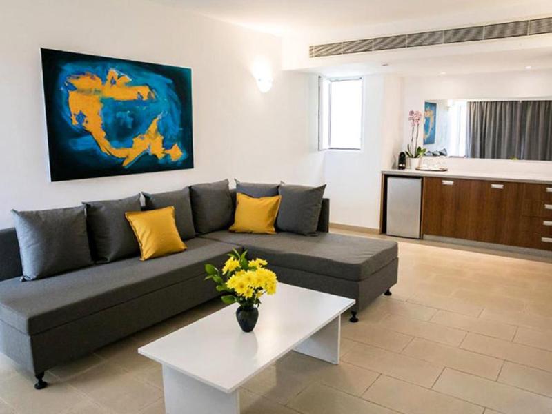 Modernes Wohnzimmer mit graßer grauer Couch, gelben Kissen, weißem Tisch und abstraktem Wandbild.