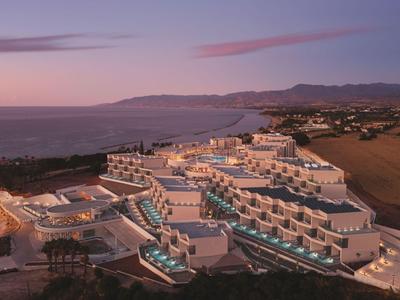 Hôtel de luxe avec piscines au bord de la mer dans un paysage vallonné au coucher du soleil.