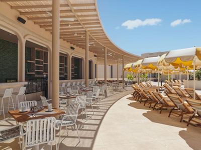 Terrasse extérieure d'hôtel avec tables, chaises, transats et ciel bleu.