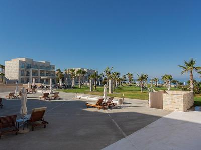 Moderner Hotelkomplex mit Liegestühlen, Sonnenschirmen und Palmen im Außenbereich.