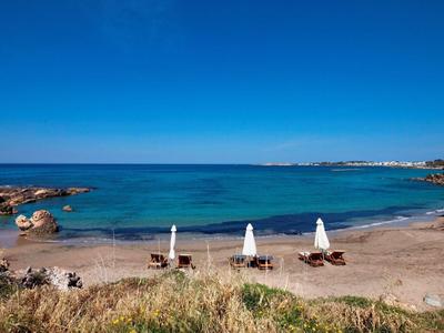 Strand mit Liegestühlen und Sonnenschirmen vor klarem, blauem Meer und wolkenlosem Himmel.