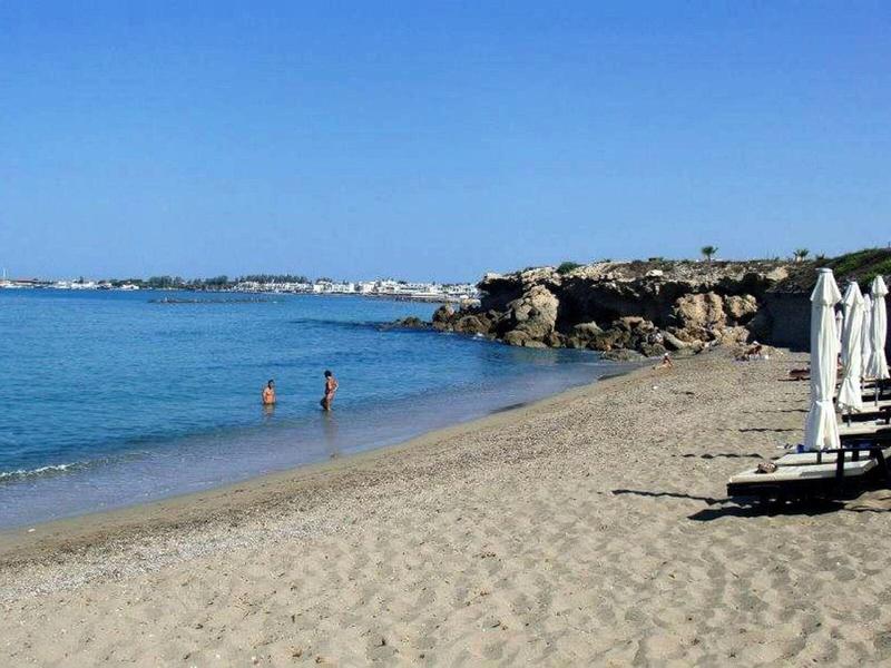 Sandstrand mit mehreren Sonnenschirmen und zwei Personen im seichten Wasser