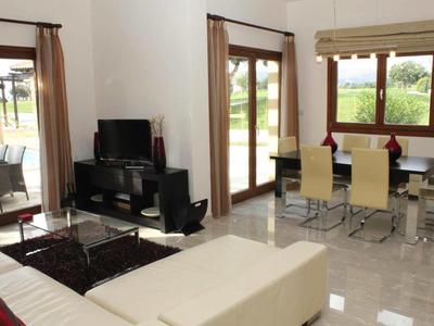 Helles Wohnzimmer mit beigem Sofa, TV, Esstisch und großen Fenstern mit Blick ins Grüne.