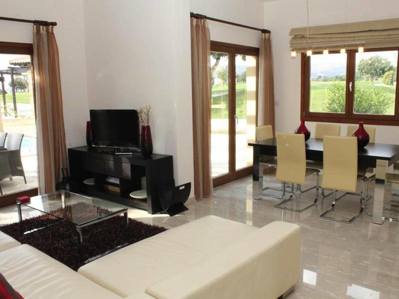 Moderner Wohn- und Essbereich mit hellen Fliesen, Sofa, TV und großen Fenstern mit braunen Vorhängen.