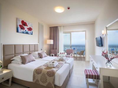 Světle zařízený hotelový pokoj s manželskou postelí, balkonem a moderním vybavením.