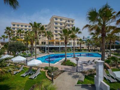 Hotel s venkovním bazénem, lehátky a palmami pod modrou oblohou.