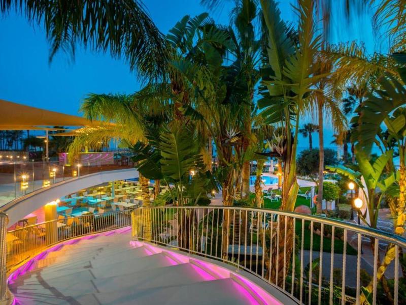 Abendliche Hotelterrasse mit bunten Lichtern, Palmen und gedeckten Tischen im Freien.