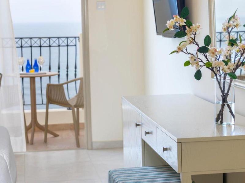 Helles Zimmer mit weißem Schreibtisch, Blumenvase und Balkon mit Stühlen und Tisch.