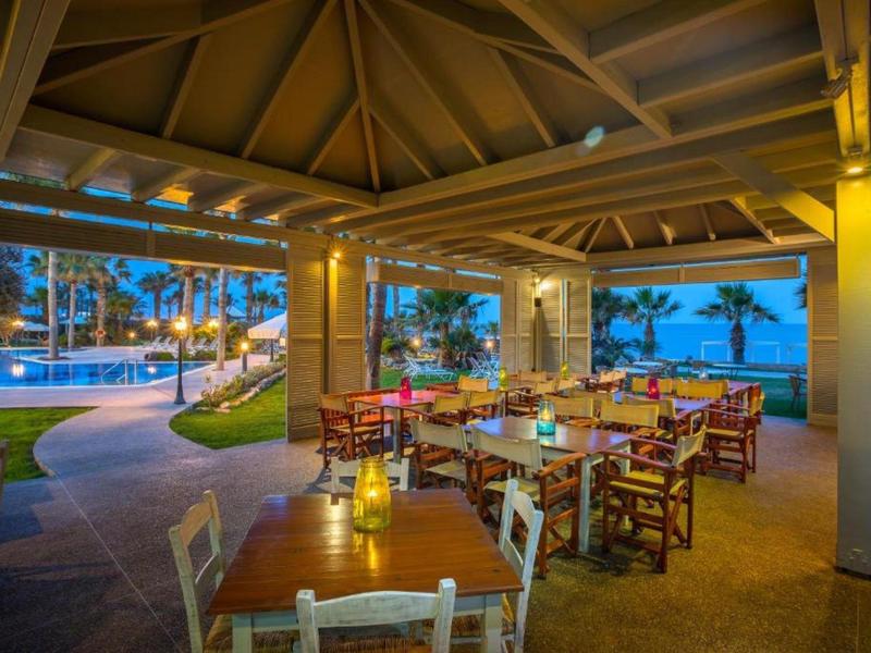 Offener Pavillon mit gedeckten Tischen und Holzstühlen, Blick auf beleuchteten Pool und Palmen.