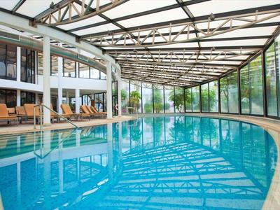 Innenpool mit blauem Wasser in einem modernen Hotel mit Glasdach und Liegestühlen.