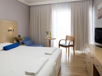 Helles Hotelzimmer mit großem Bett, Sitzbereich und TV in neutralen Farben.