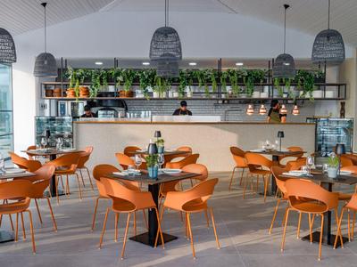 Modernes Restaurant mit orangefarbenen Stühlen, Holztischen und einer grünen Pflanzenwand hinter der Bar.