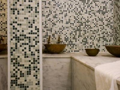 Moderner Wellnessbereich mit Mosaikfliesen, Marmorbänken, Schalen und weißen Handtüchern.