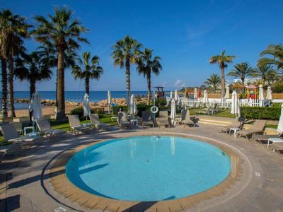 Kleiner runder Pool mit Liegestühlen und Palmen am Strand unter blauem Himmel.