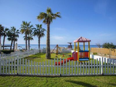 Spielplatz mit buntem Klettergerüst und Palmen am Meer bei klarem Himmel.