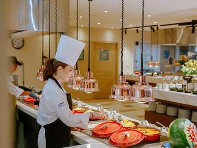 Hotelküche mit Köchin, die Gerichte auf einer Theke mit roten Tellern vorbereitet.