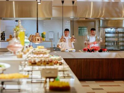 Moderne Hotelküche mit zwei Köchen und vielfältigem Buffet im Vordergrund.