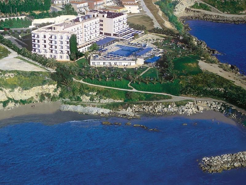 Großes Hotelgebäude nahe Küste mit Swimmingpool, Strand und blauer Meereslandschaft in sonniger Umgebung.