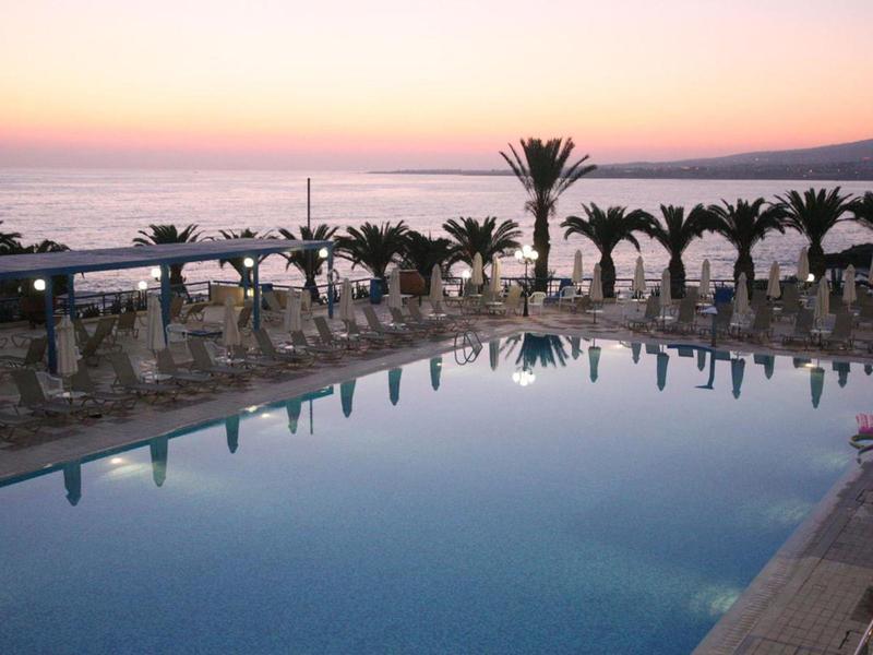 Großer Pool am Meer mit Palmen und Liegestühlen bei Sonnenuntergang.
